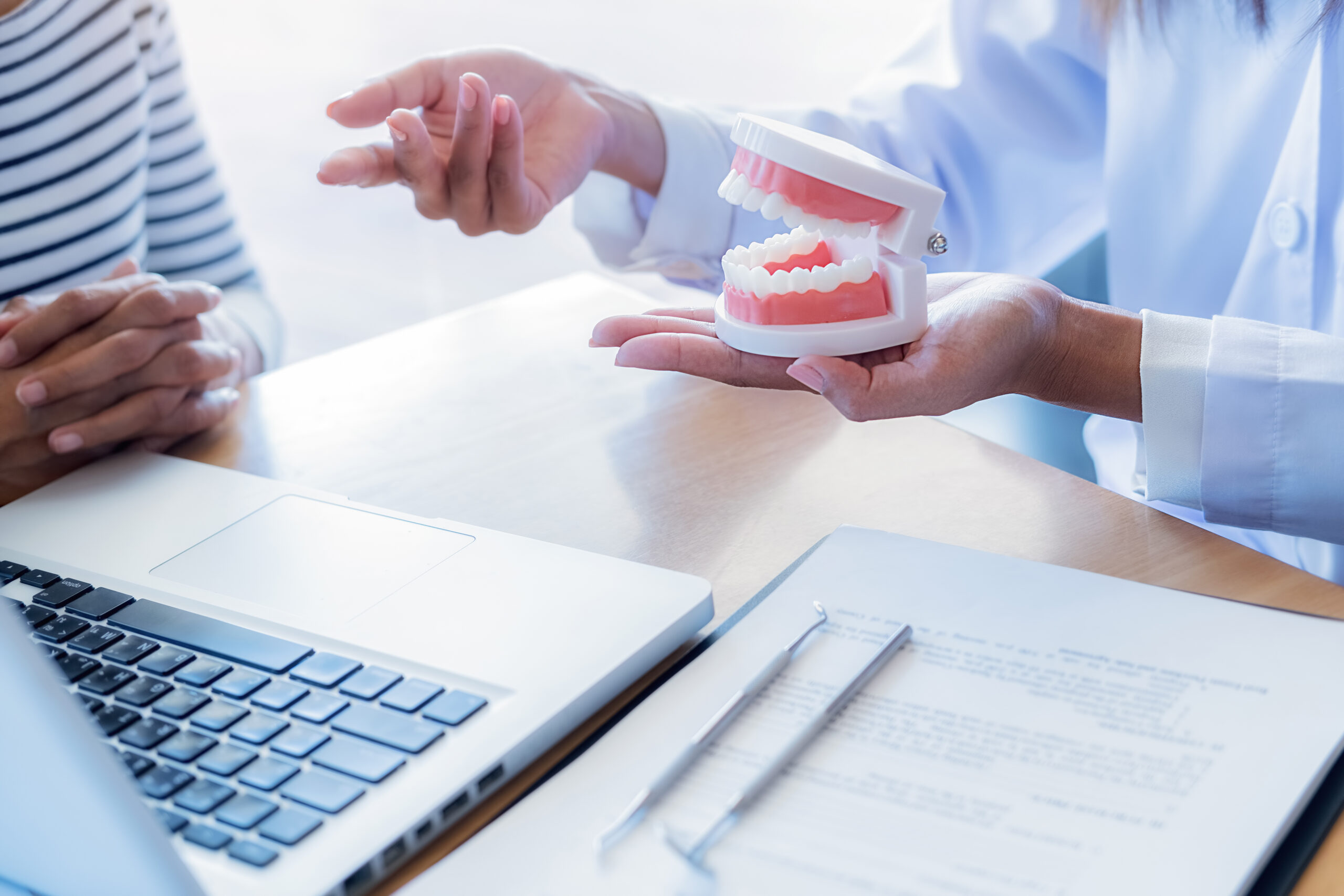 Dentist showing and explaining teeth disease treatment to patient using teeth model denture and explorer mirror tool in dental clinic office. Healthcare concept. 診療